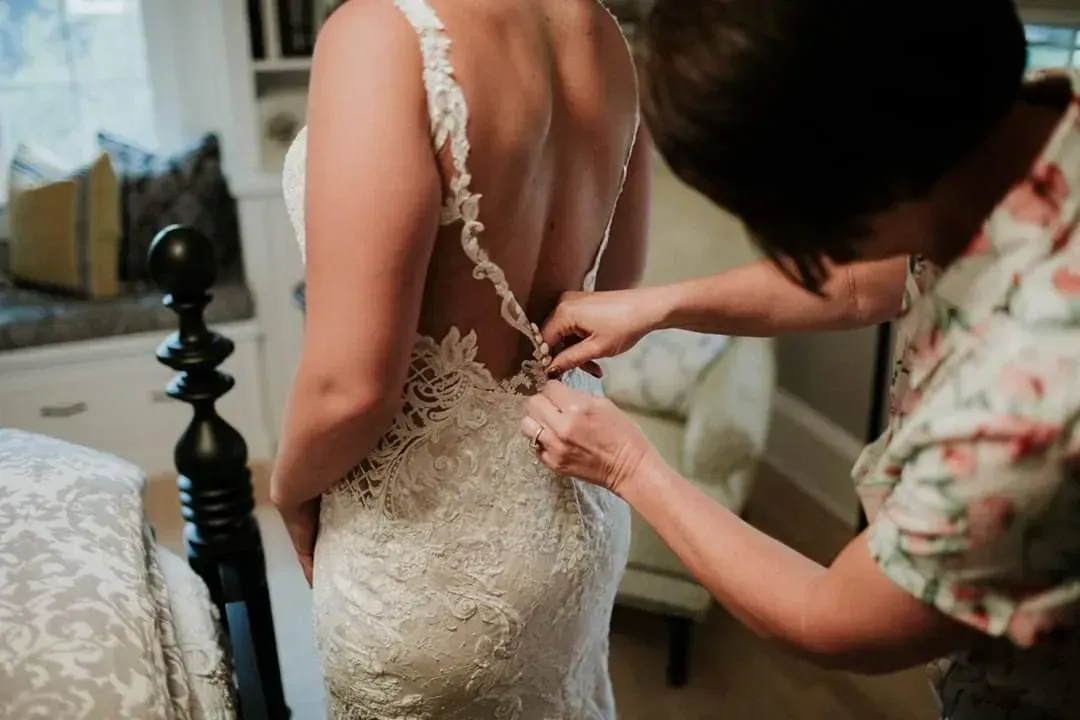 A woman is helping a woman put on her wedding dress