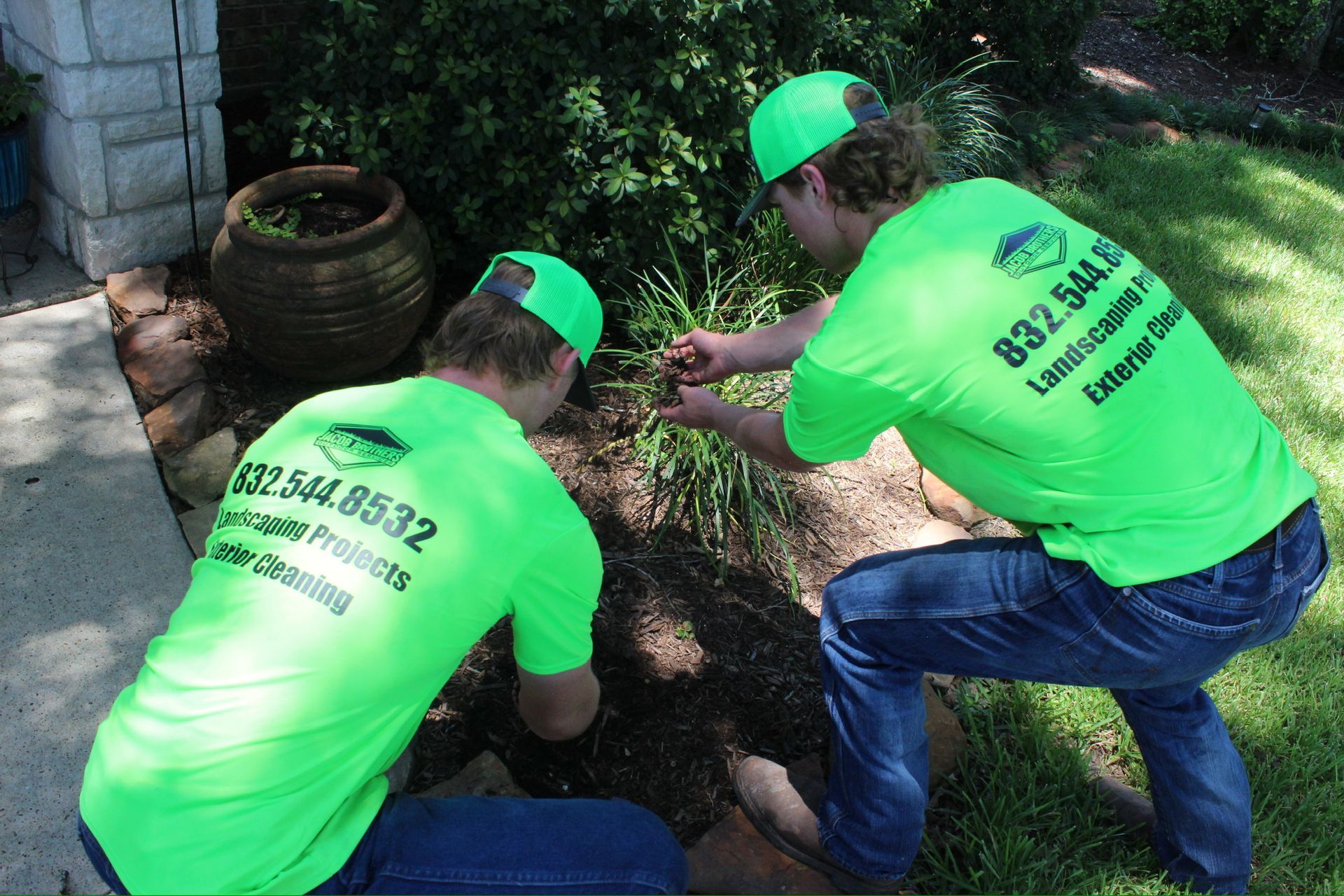 Two men wearing neon green shirts and hats are working in a garden