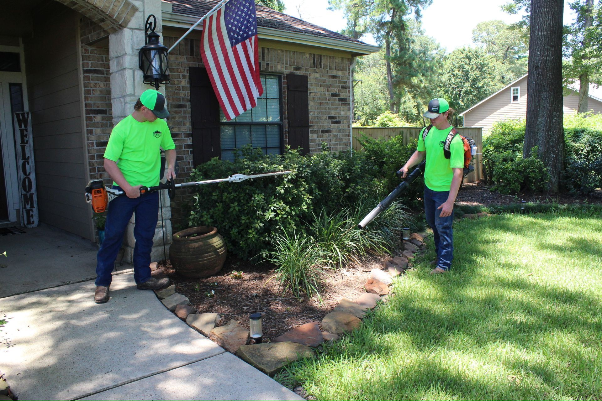 Two men in green shirts are standing in front of a house with an american flag.