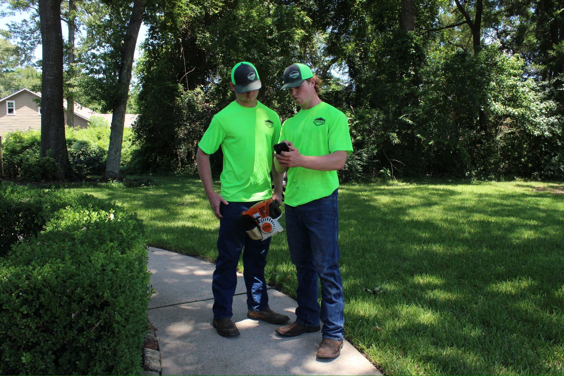 Two men in neon green shirts are standing next to each other on a sidewalk.