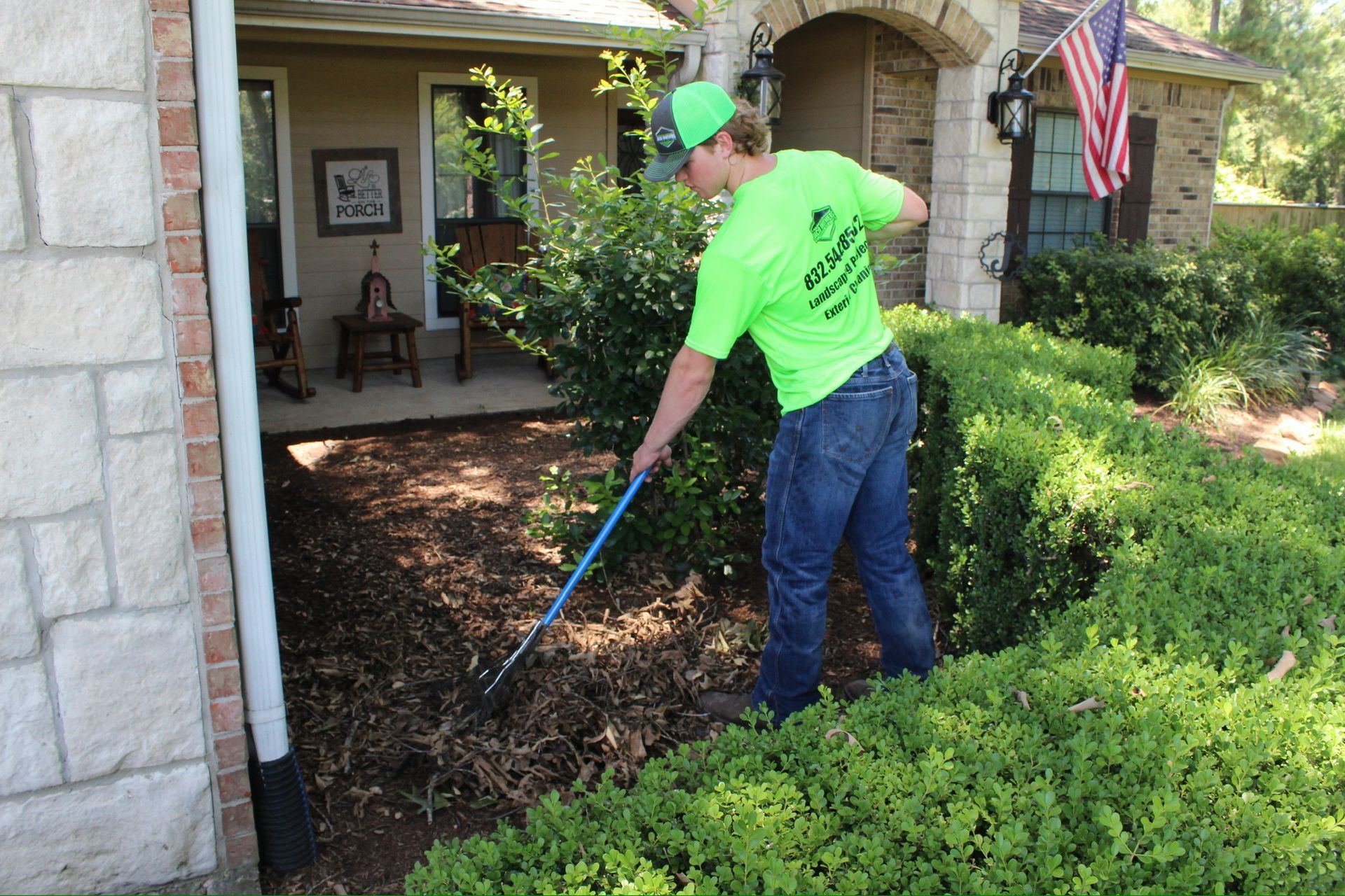 A man in a green shirt is raking a bush