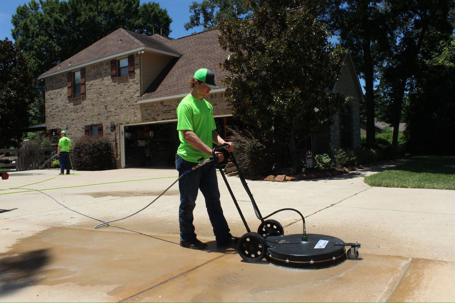 A man in a green shirt is using a machine to clean a driveway.