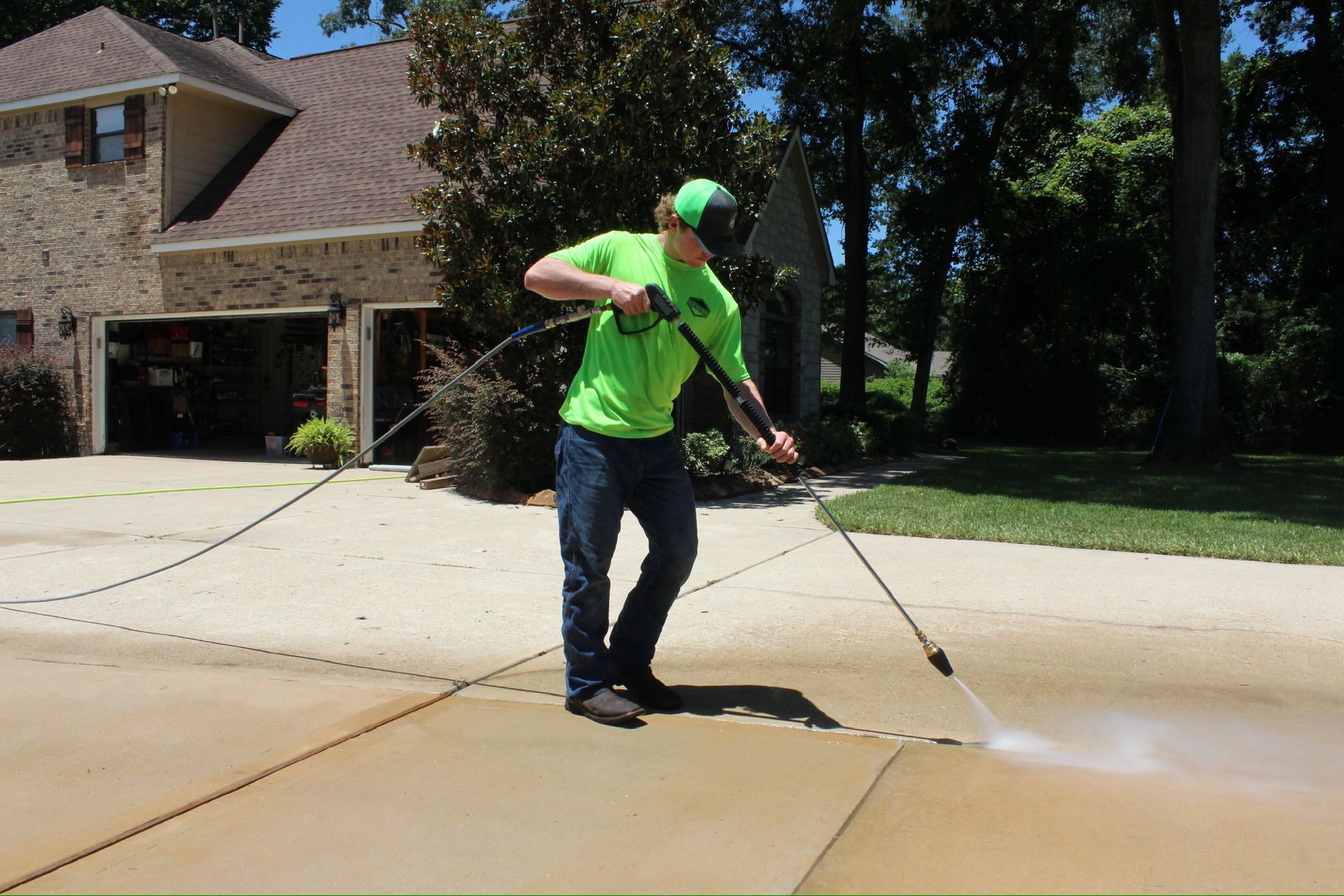 A man in a green shirt is using a high pressure washer to clean a driveway.