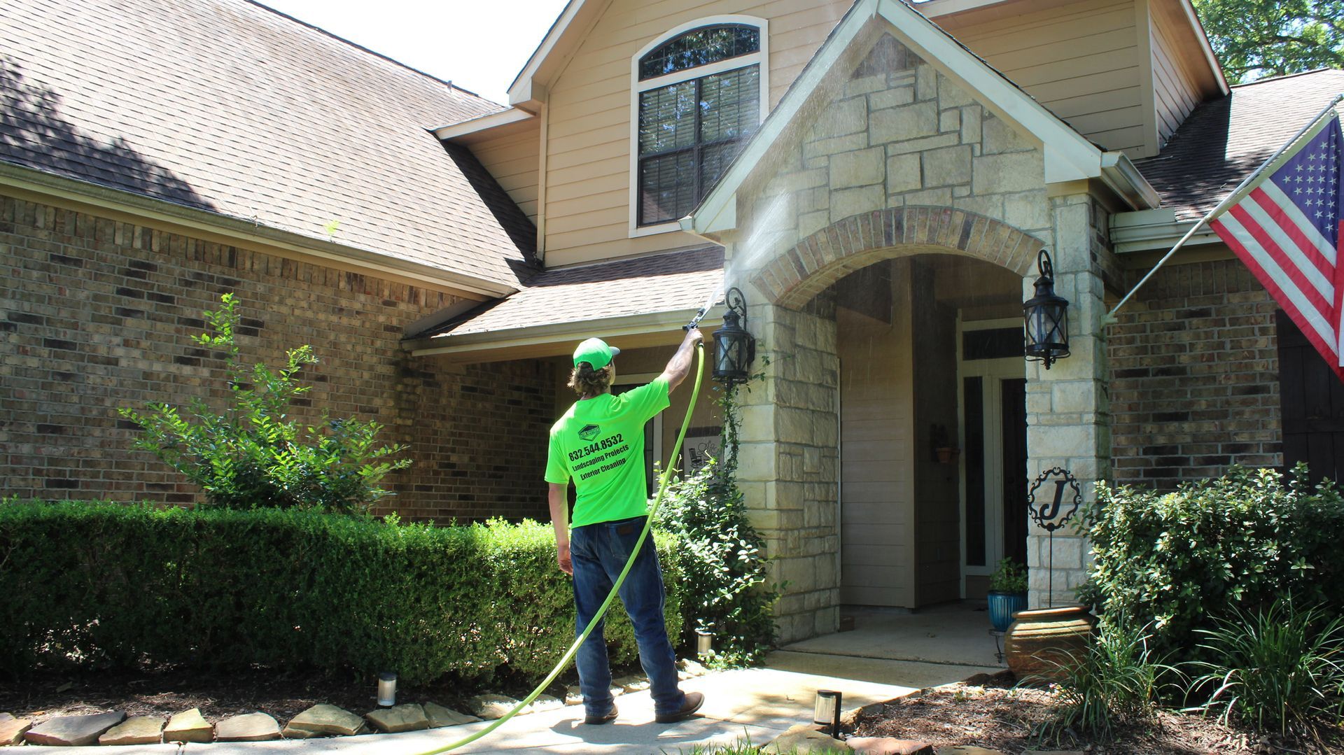 A man is cleaning the front of a house with a hose.
