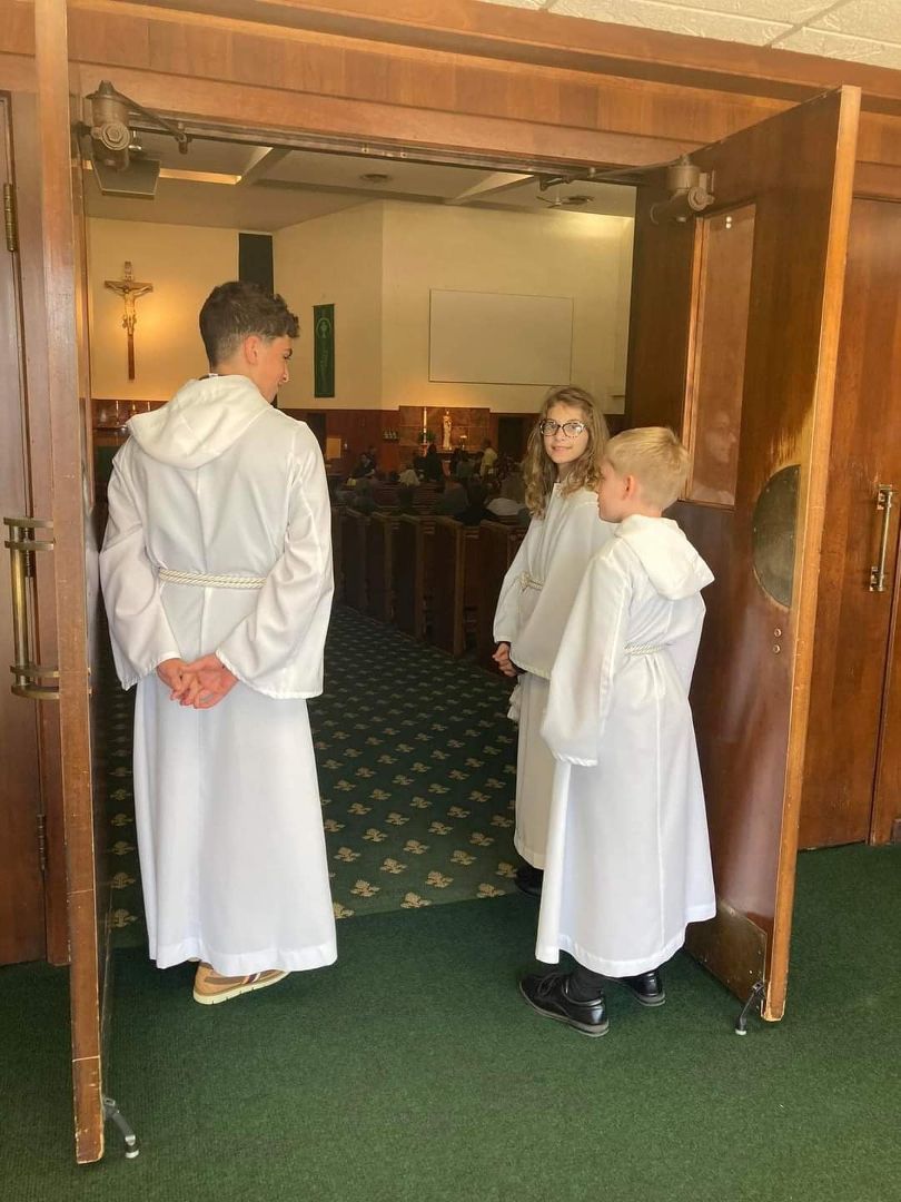 Three children in white robes are standing in a church doorway