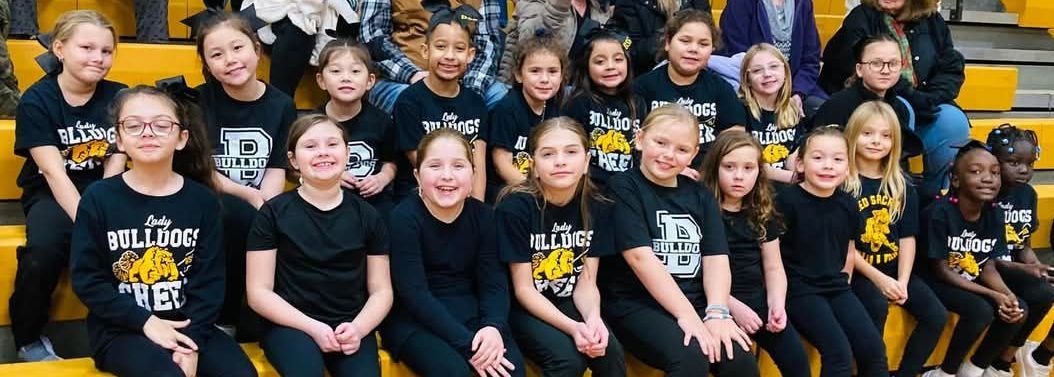 A man in a bulldogs shirt is standing next to a mascot holding a basketball.