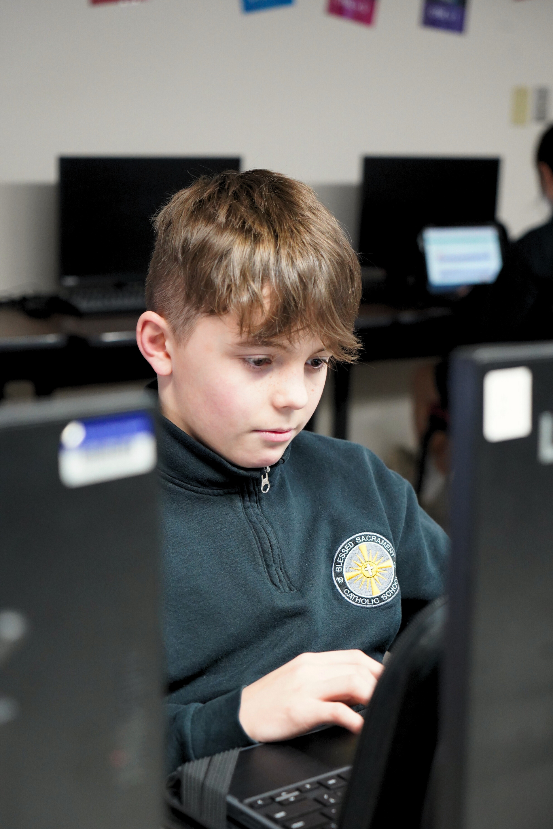 A young boy is using a laptop computer in a classroom.