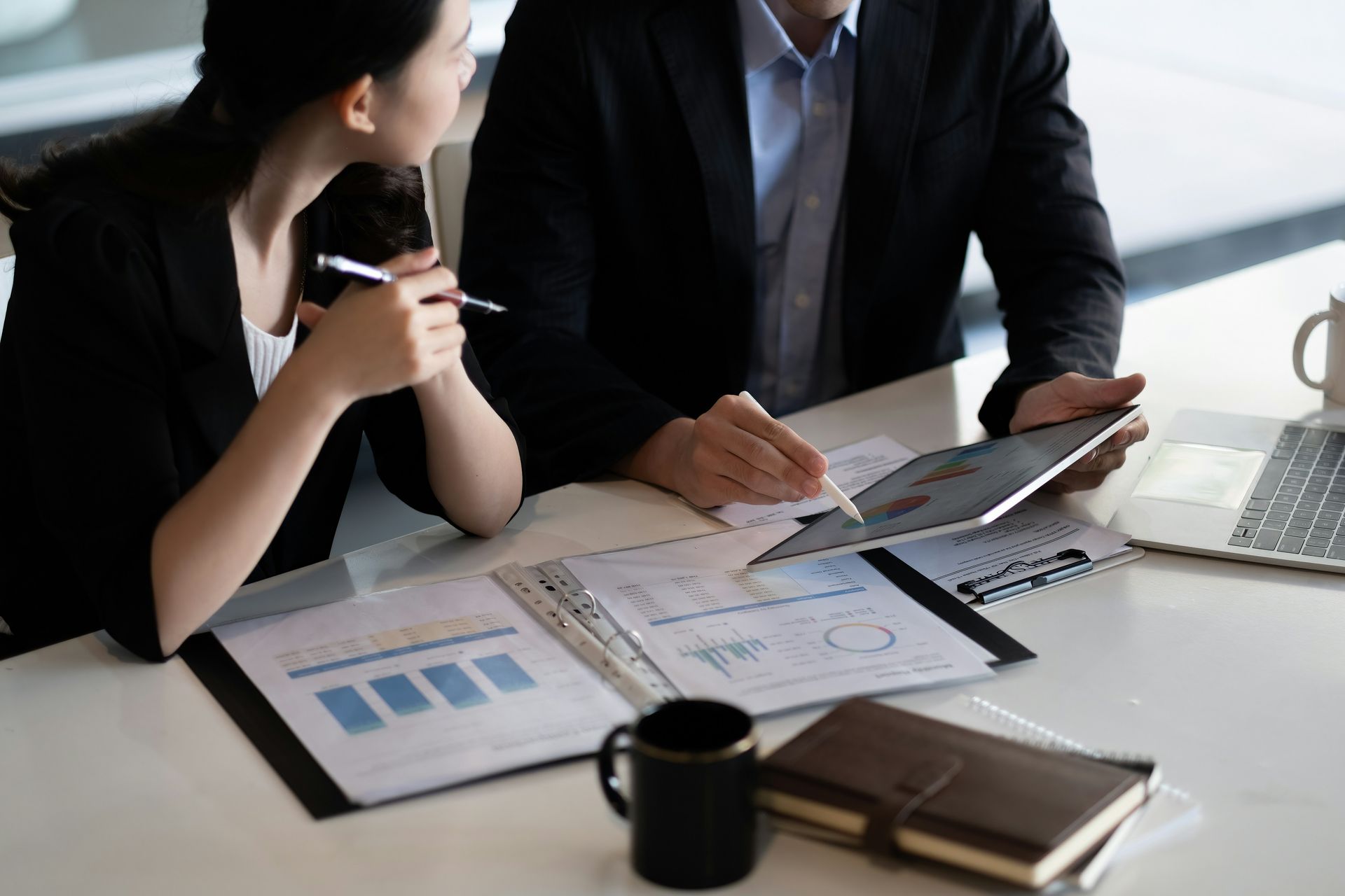 A man and a woman are sitting at a table looking at a tablet.