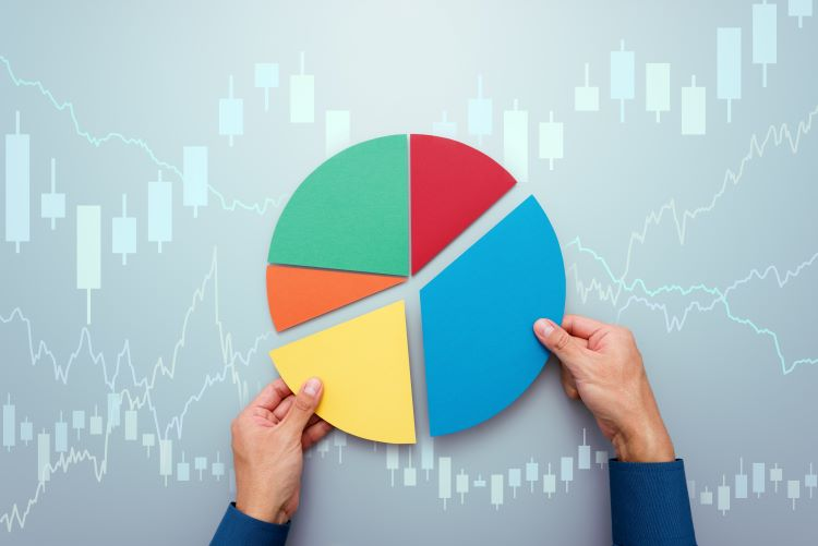 A person is holding a colorful pie chart in front of a stock chart.