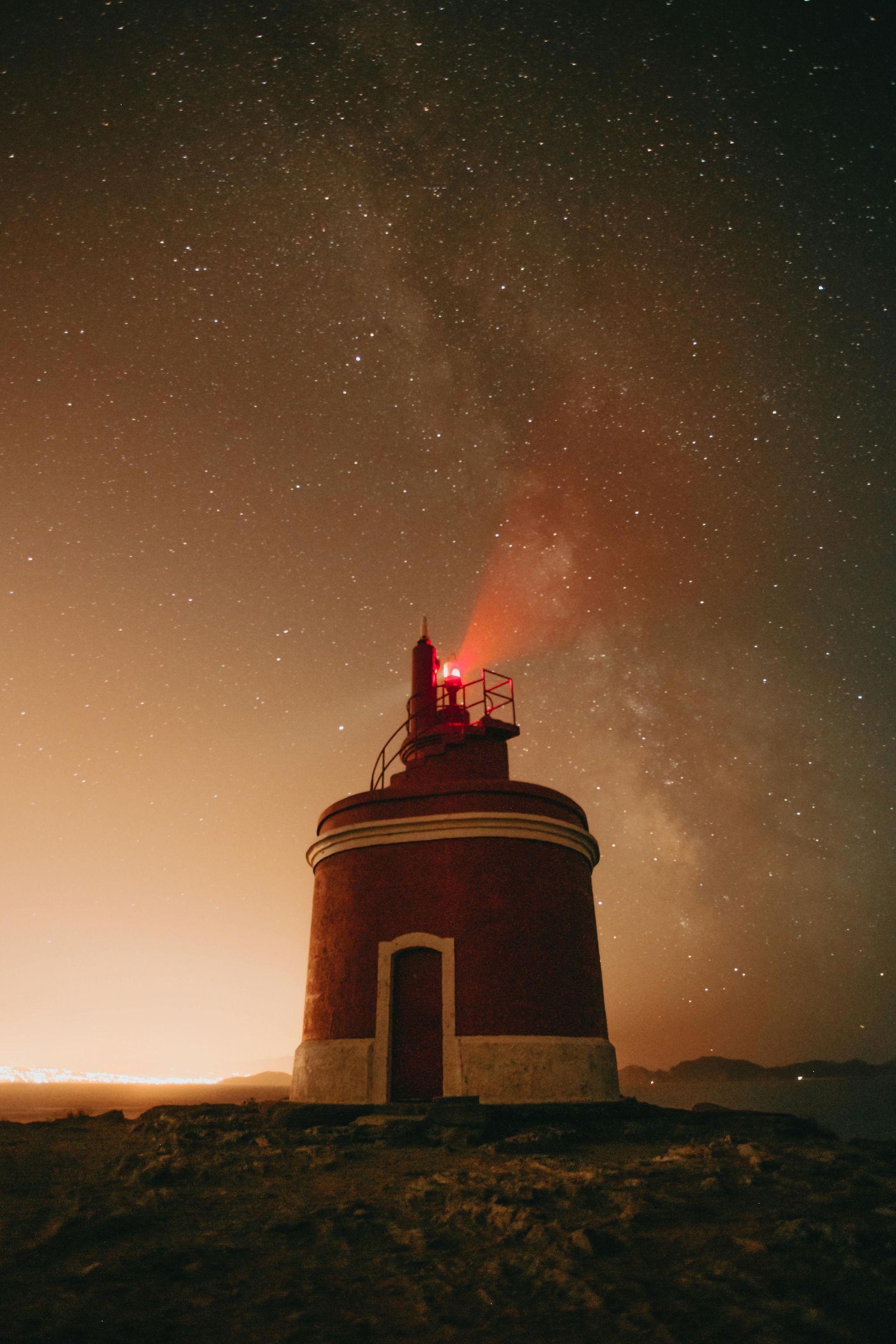 A lighthouse is lit up at night under a starry sky.