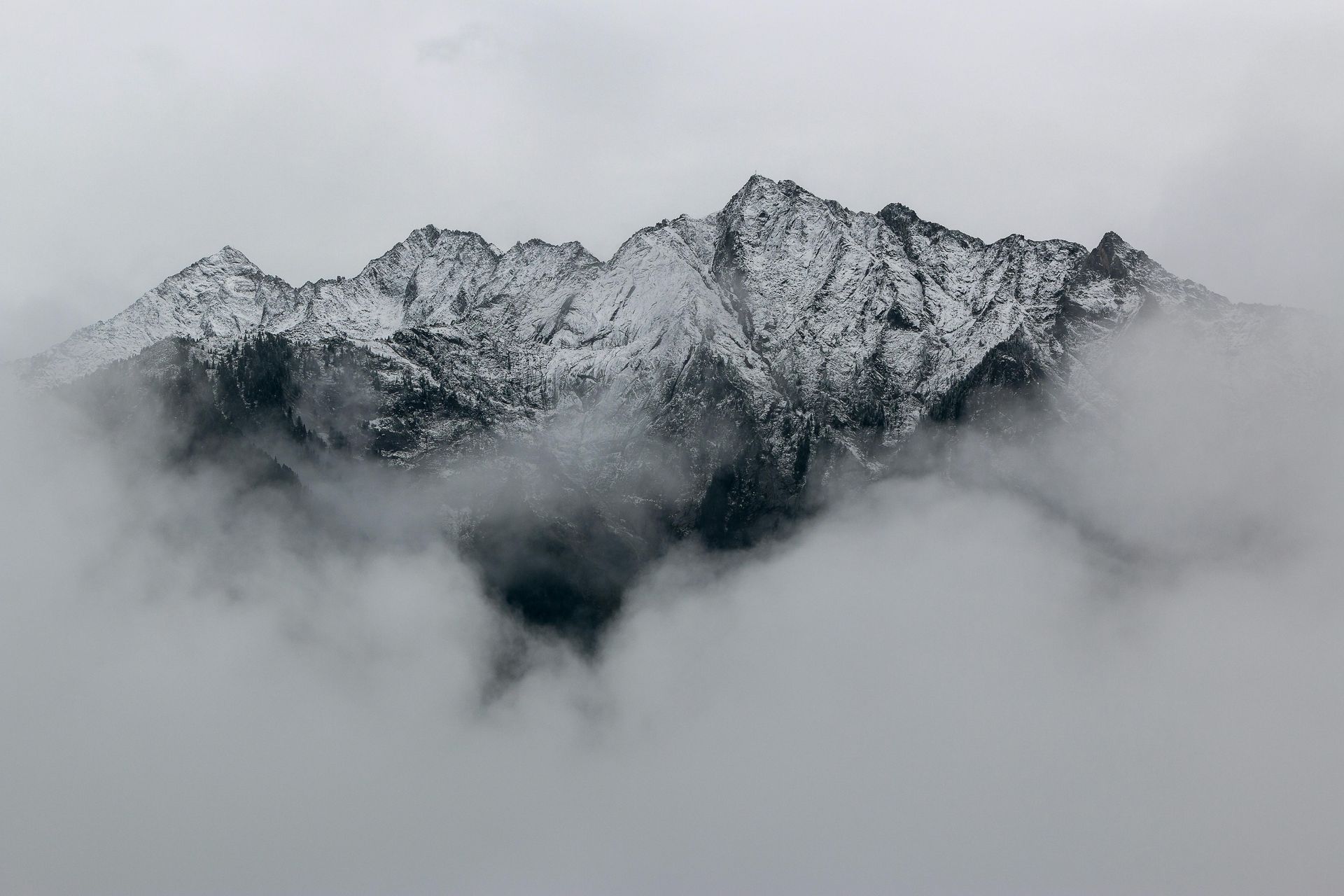 A black and white photo of a snowy mountain surrounded by clouds.