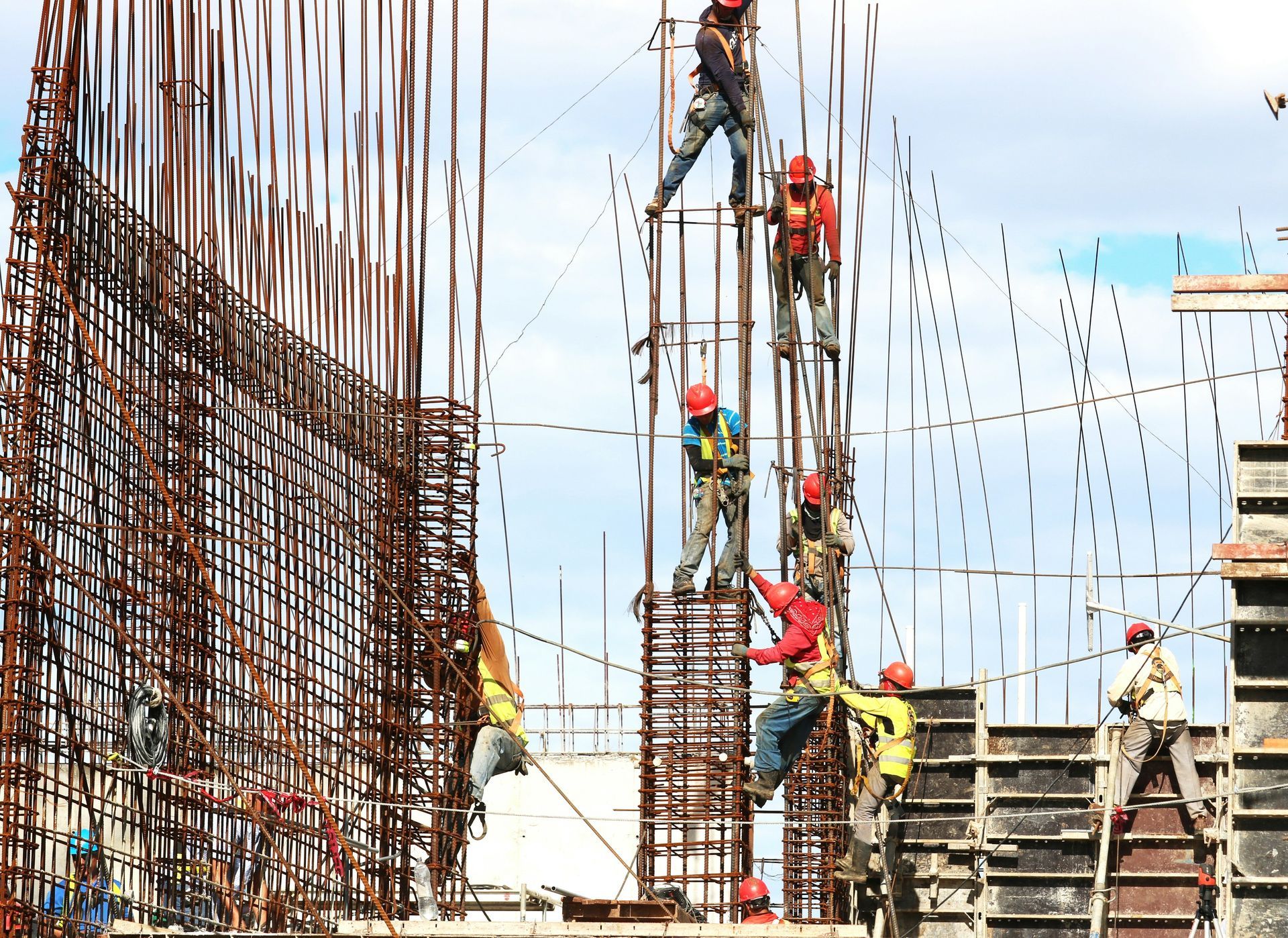 Construction workers on steel rebar scaffolding at a building site under a bright sky