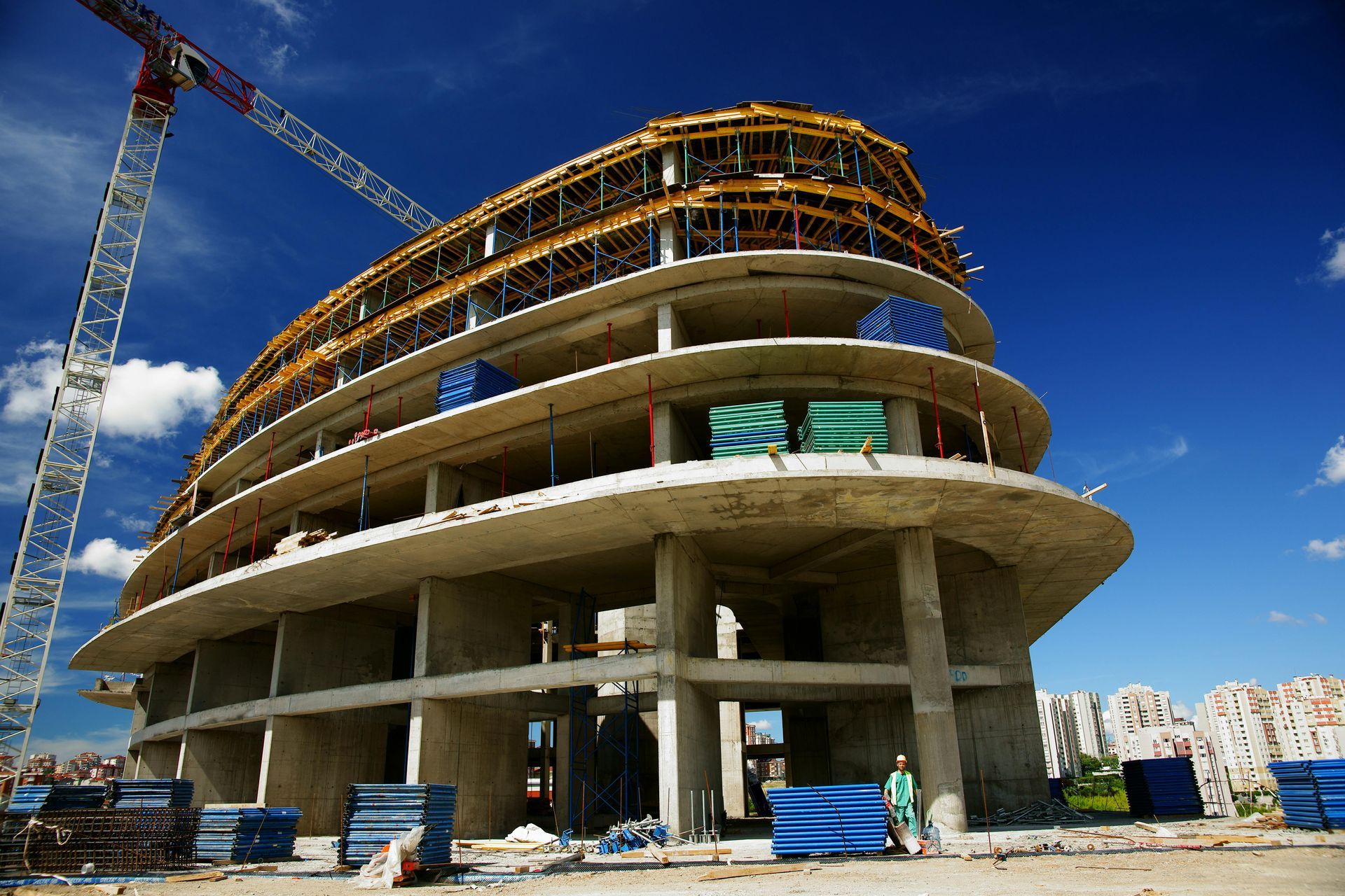 Curved concrete building under construction with a crane and workers against a blue sky