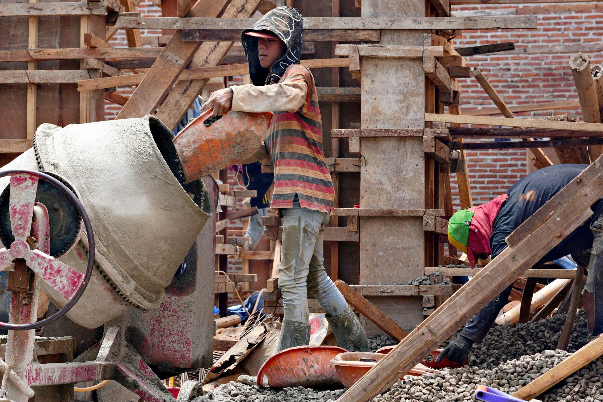 Workers mixing concrete at a construction site with brick walls and wooden scaffolding