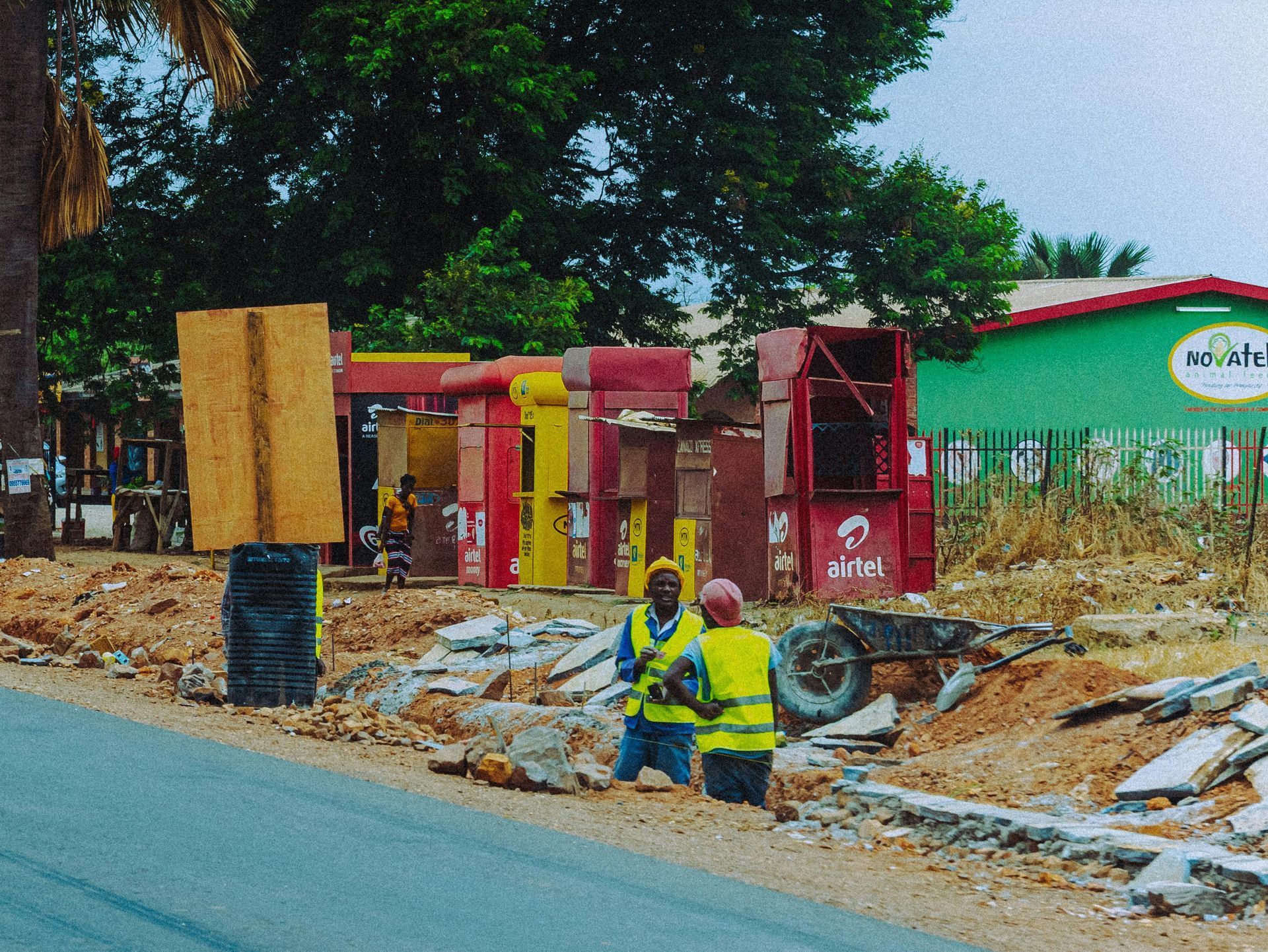 Roadside utility work with workers in yellow vests beside a street and red equipment booths