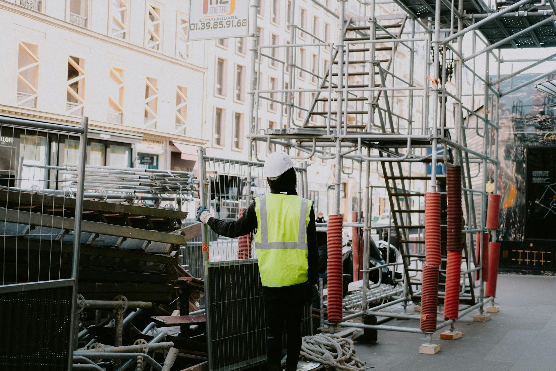 Construction worker in a yellow vest walking under scaffolding on a city street