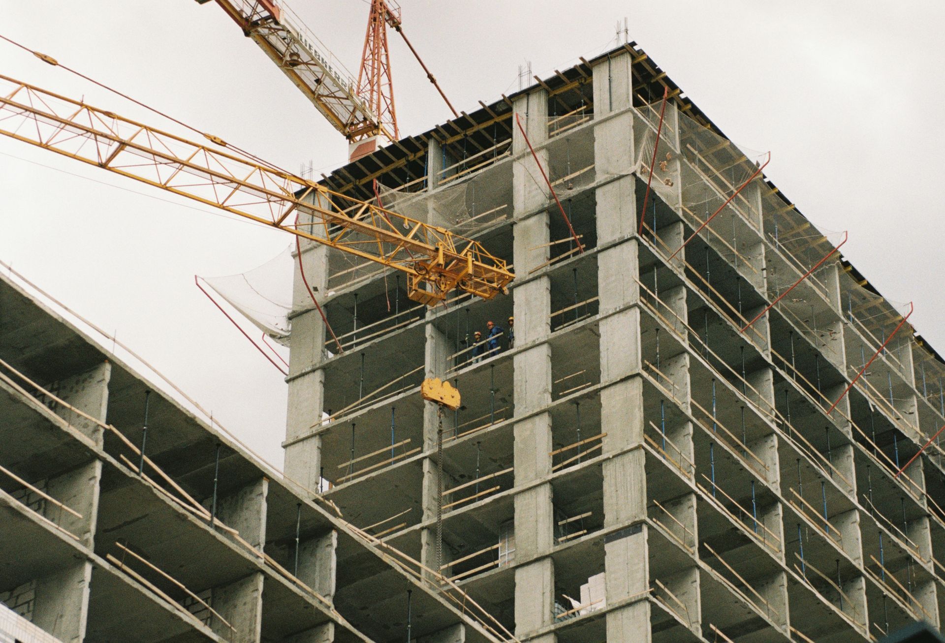High-rise building under construction with yellow cranes against a cloudy sky