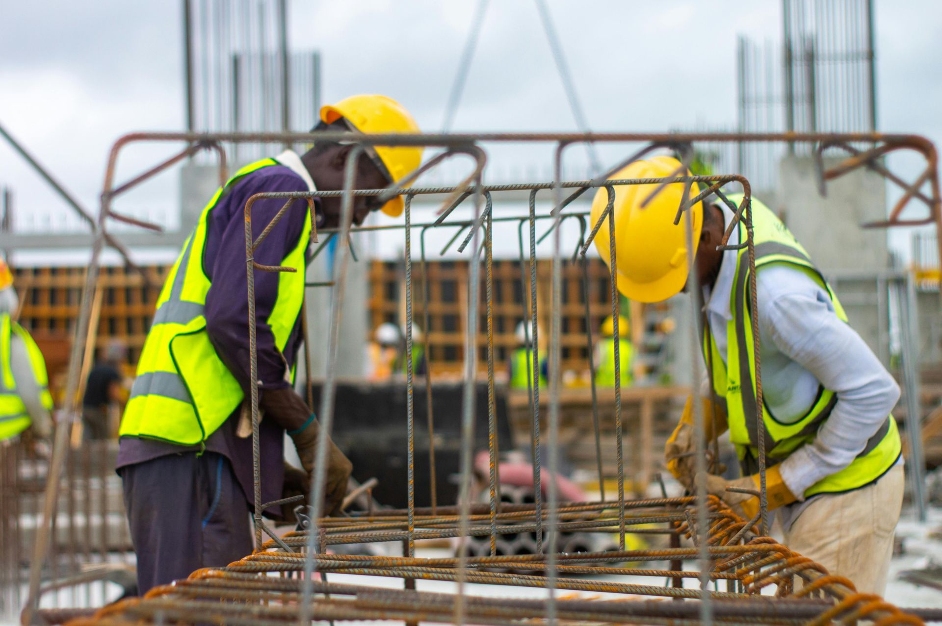 Construction workers in yellow hard hats bending over rebar at a building site