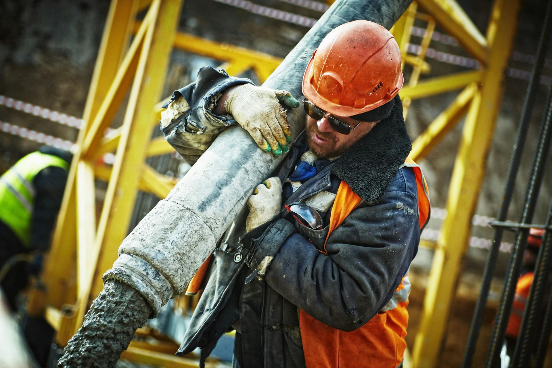 Construction worker in orange hard hat guiding a heavy pipe at an industrial worksite