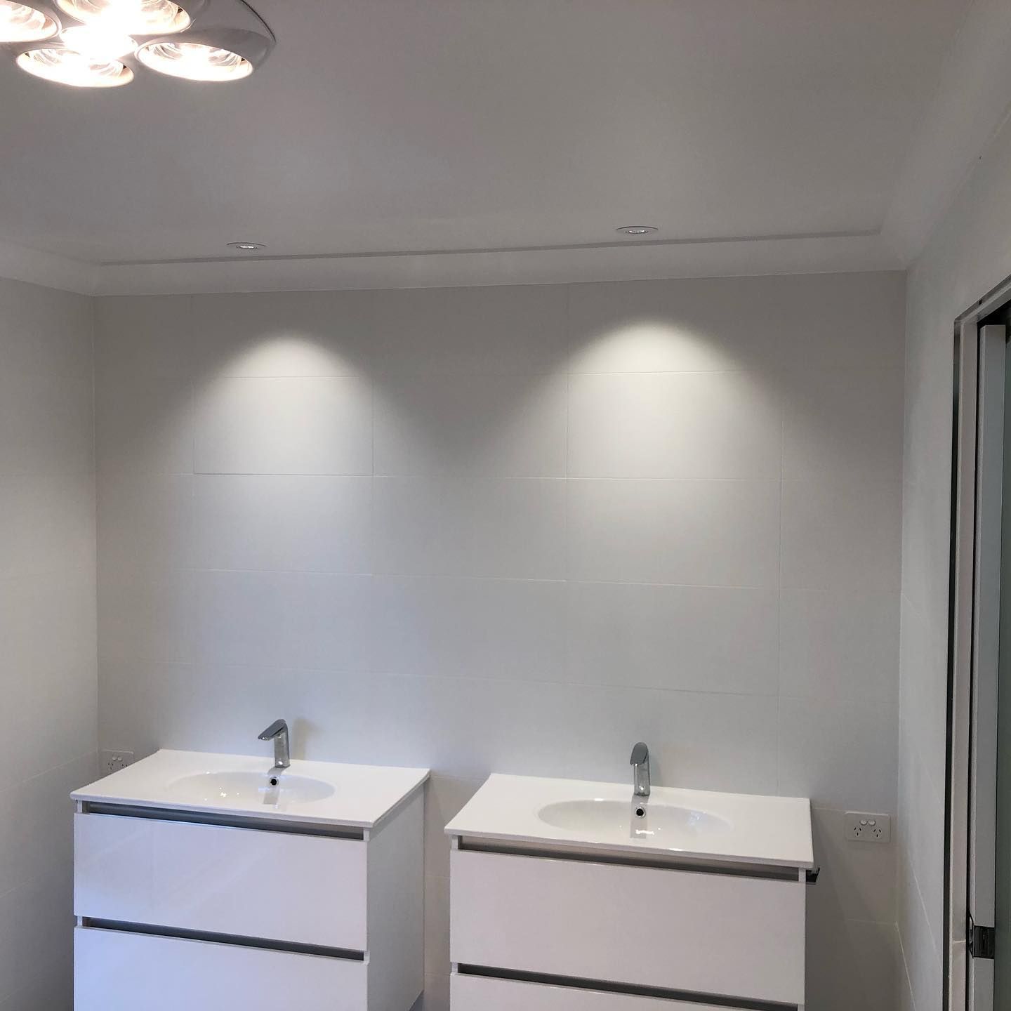 Two white bathroom vanities with sinks, under spotlighting against a white wall.