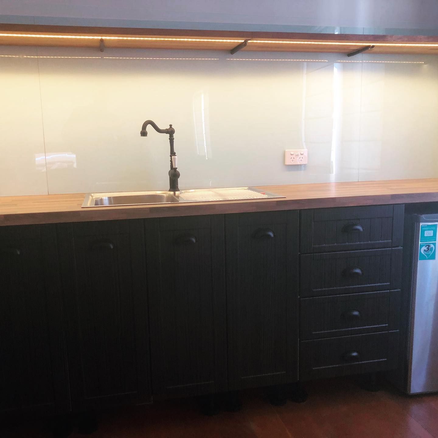 Kitchen countertop with black cabinets, faucet, and small refrigerator.