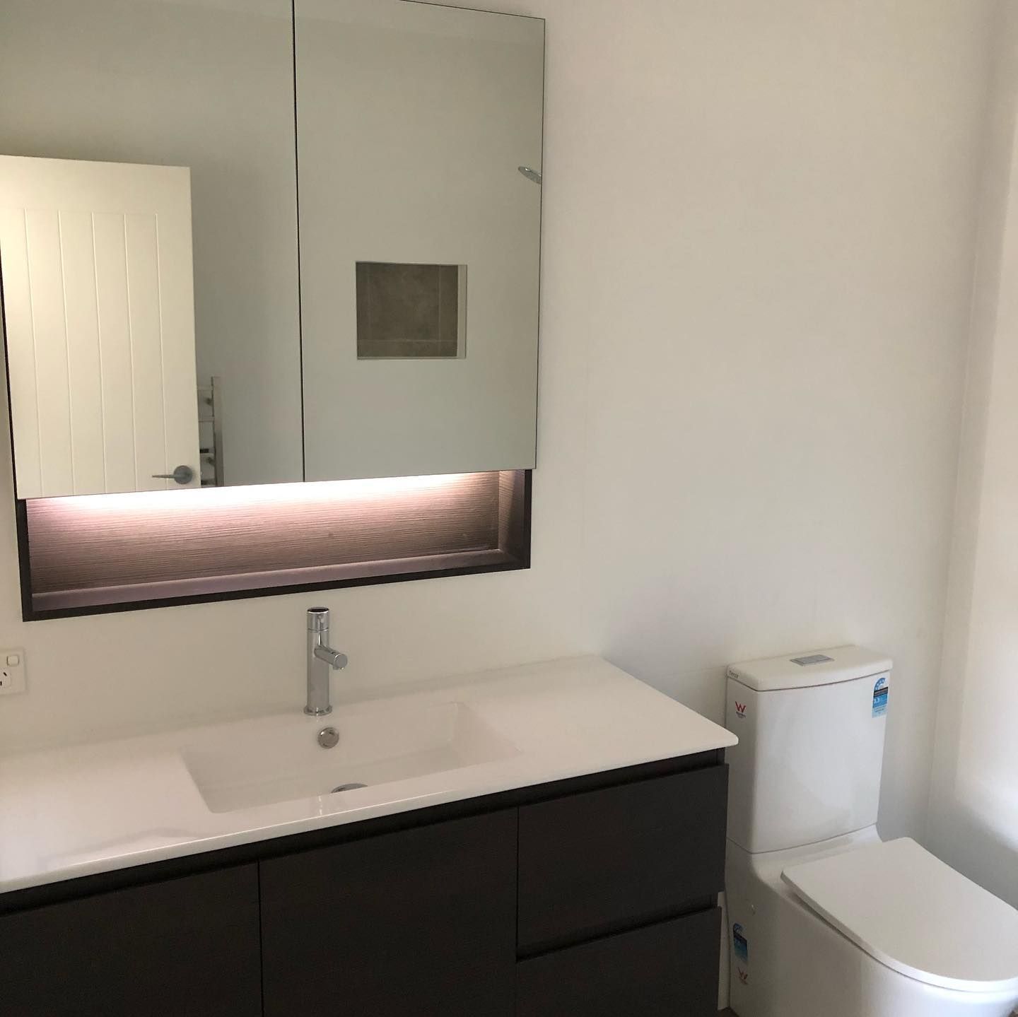 Bathroom with a vanity, large mirror, toilet, and a recessed light. Dark brown cabinetry.