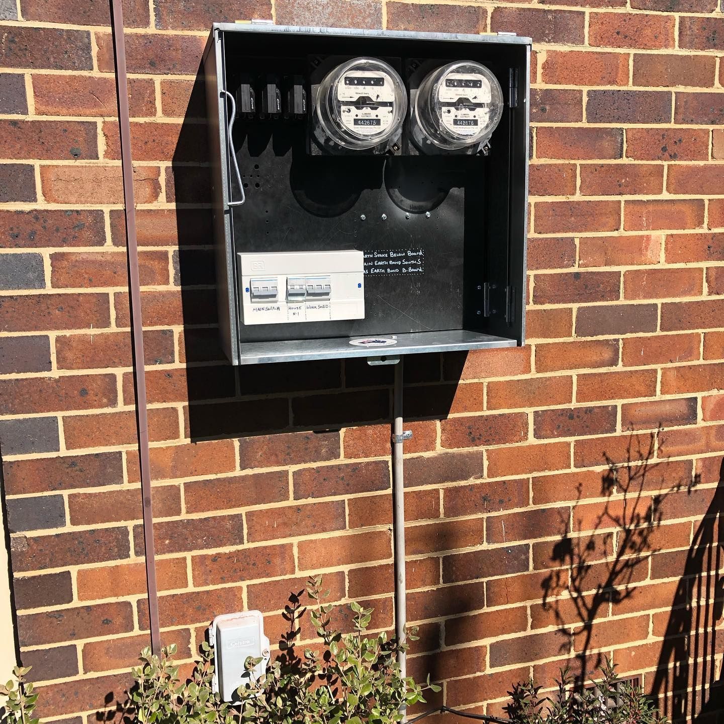 Man in work clothes uses a screwdriver on a wall plate on a white wall.