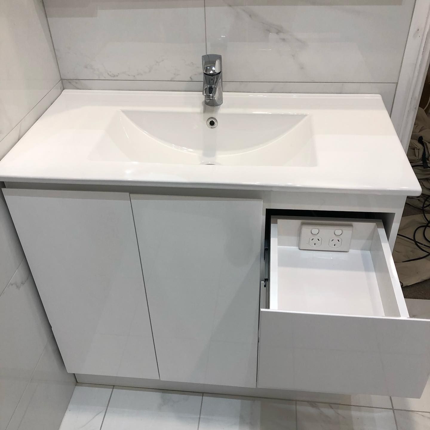 White bathroom vanity with sink, faucet, cabinet doors, and open drawer with power outlet.