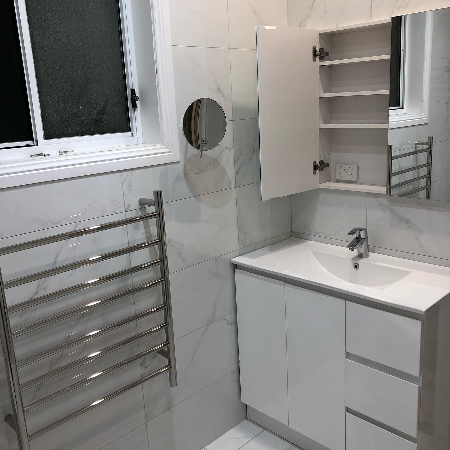 White bathroom with a heated towel rack, vanity, and medicine cabinet.