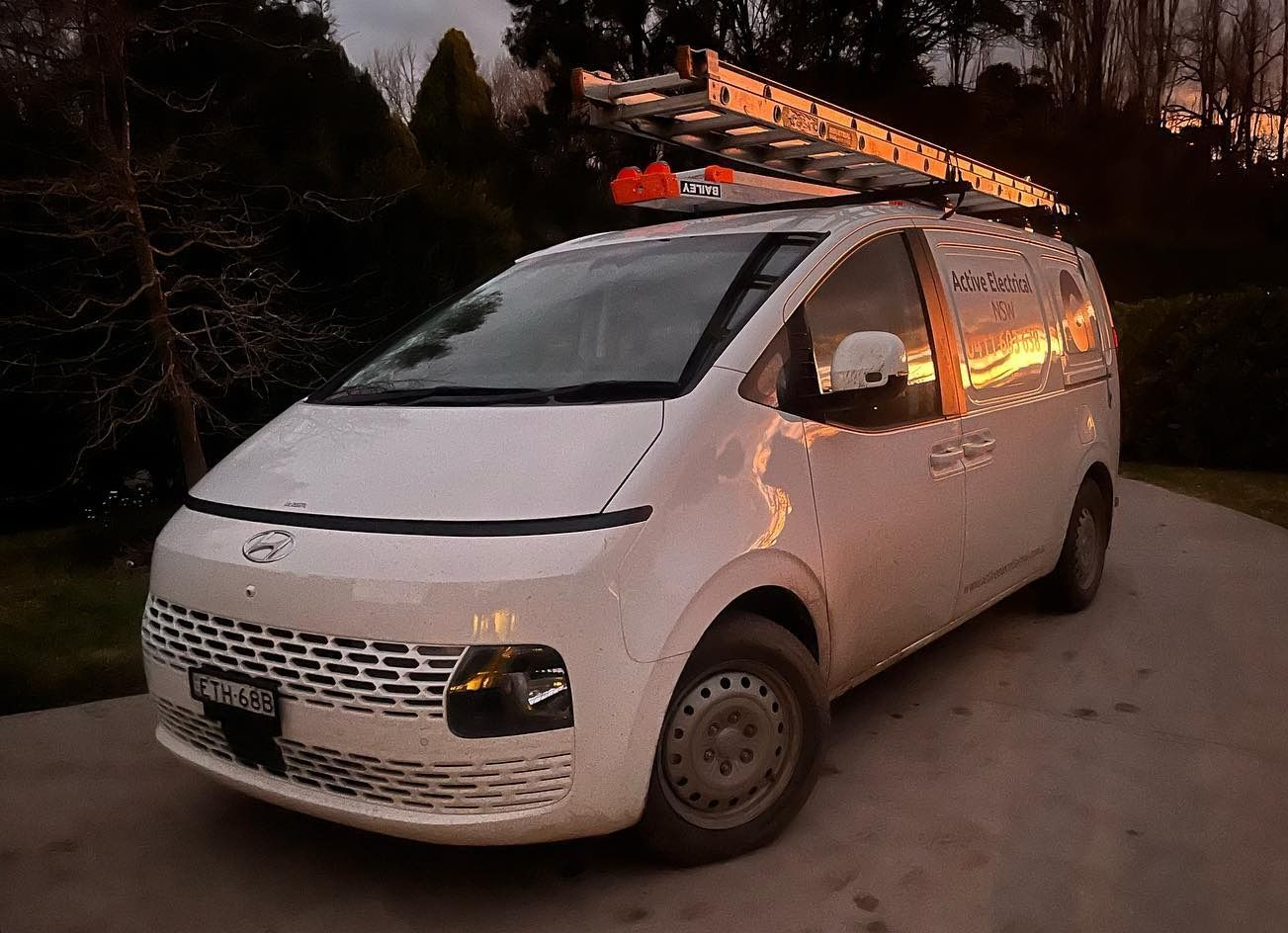 A person on a ladder installs a smoke detector on a white ceiling, with hanging lights in a room.
