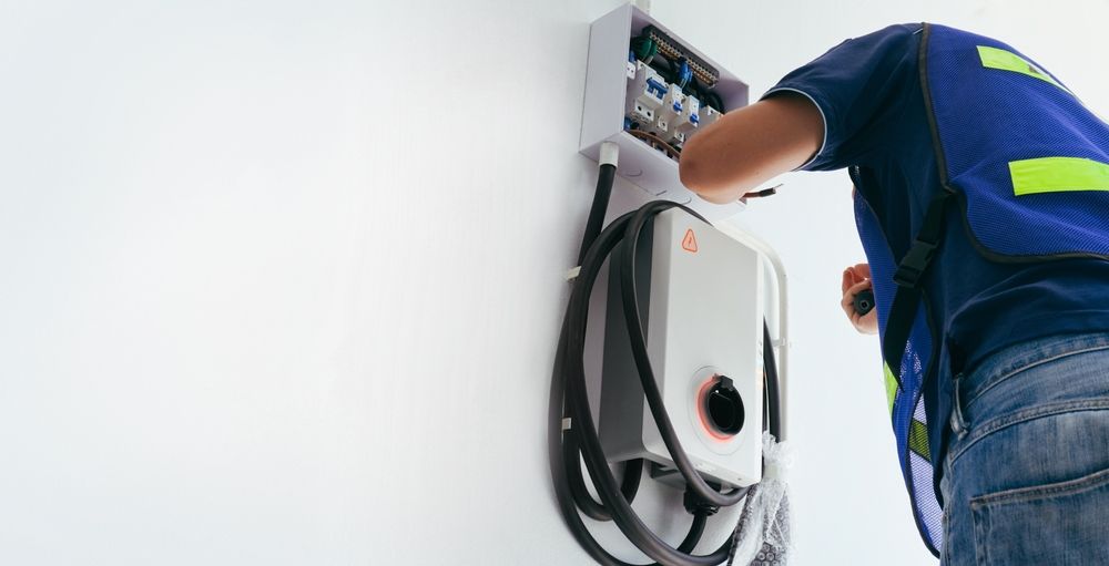 Electrician installing an EV charger on a white wall.