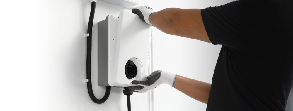 Person installing a white electrical device on a wall, wearing gloves.