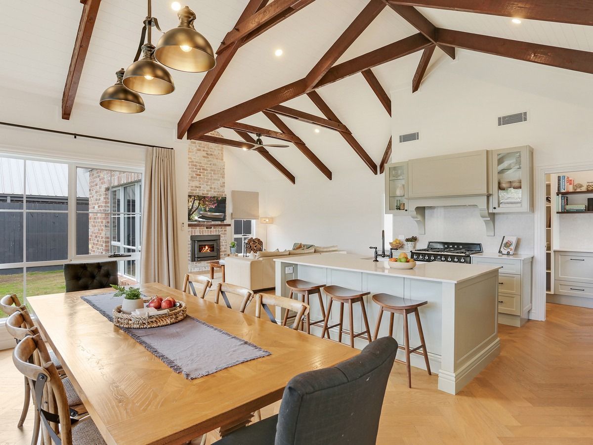 Open-plan kitchen and dining area with exposed wooden beams, pendant lights, and large dining table.