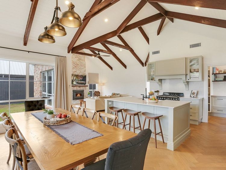 Open-plan kitchen and dining area with exposed wooden beams, pendant lights, and large dining table.