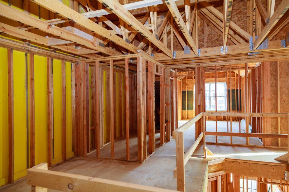 Interior of a house under construction with exposed wooden framing and yellow insulation.