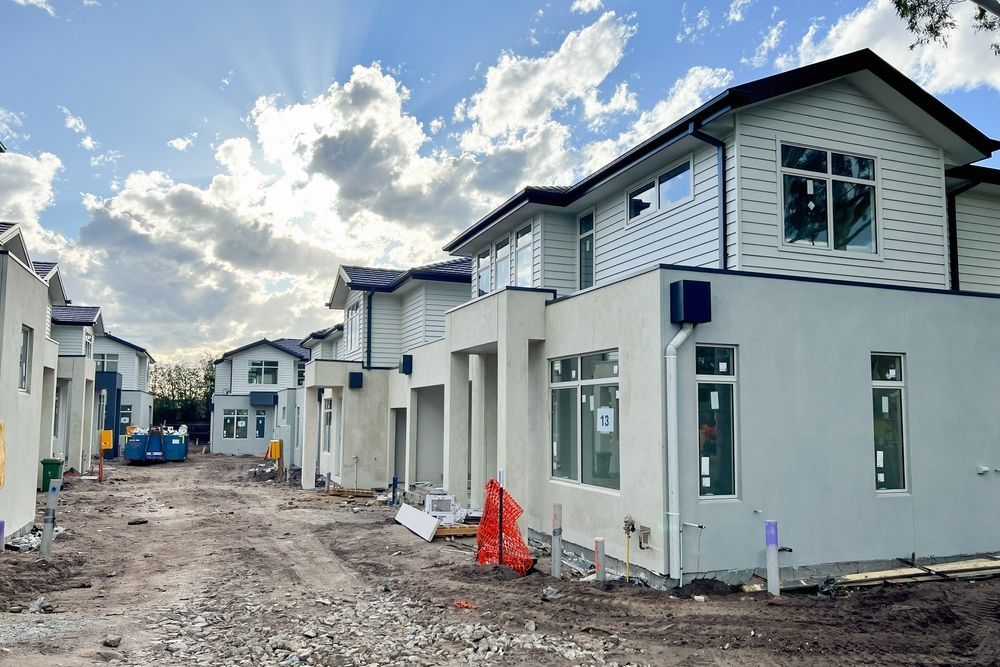 Row of newly constructed two-story houses on a dusty street under a cloudy sky.