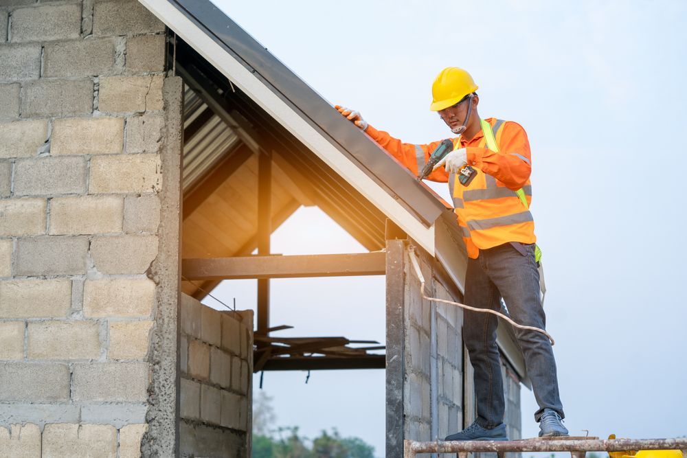 Construction worker on a ladder, installing roofing on a building under construction.