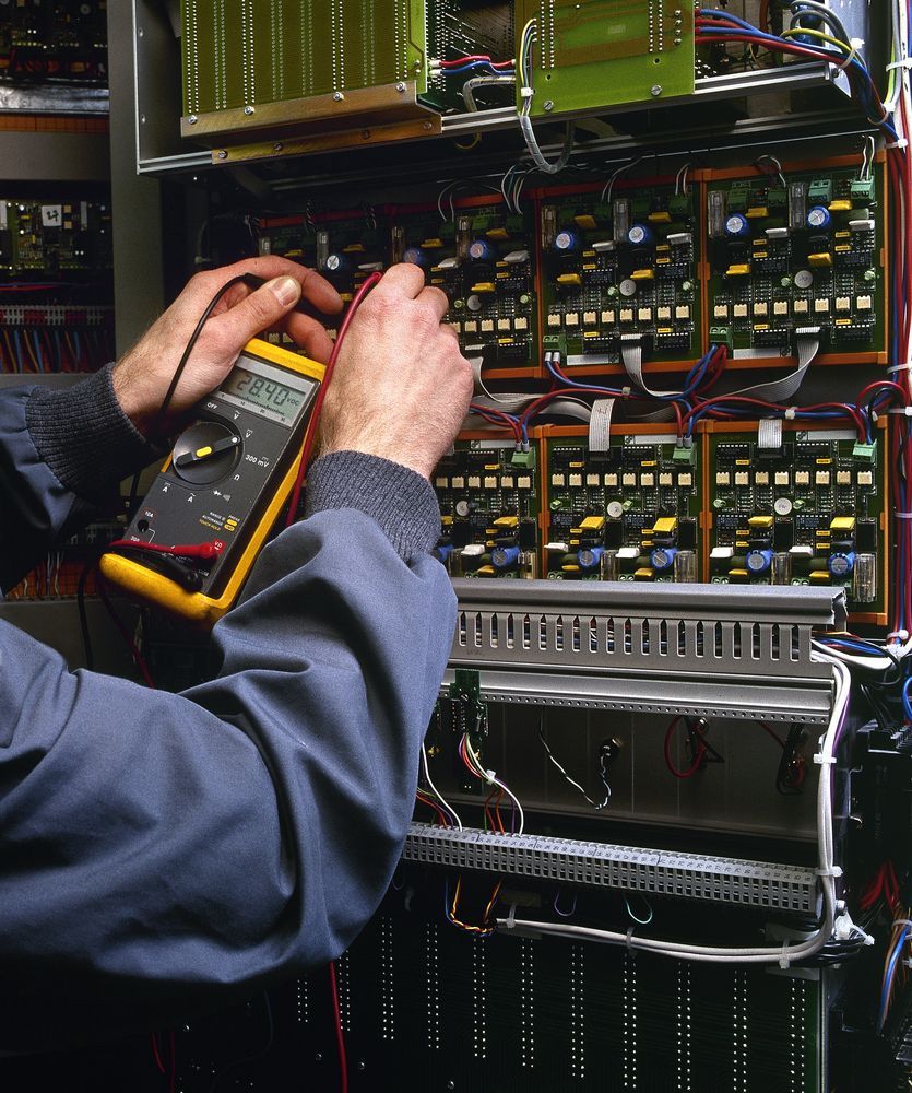 Hands testing electronics with a multimeter in a server rack.