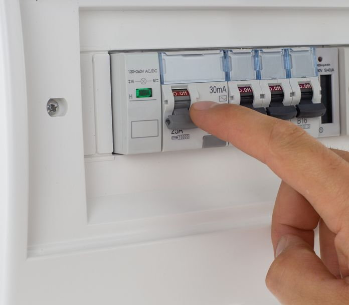 Hand flipping a circuit breaker switch in a white electrical panel.
