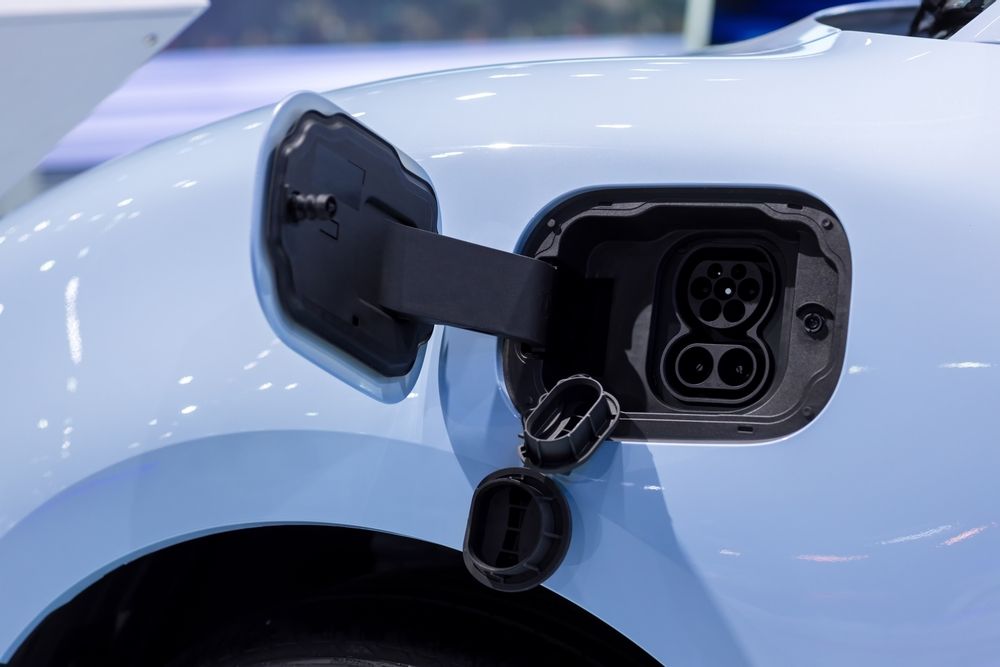 Open charging port on a light blue electric car, showing multiple connector sockets.