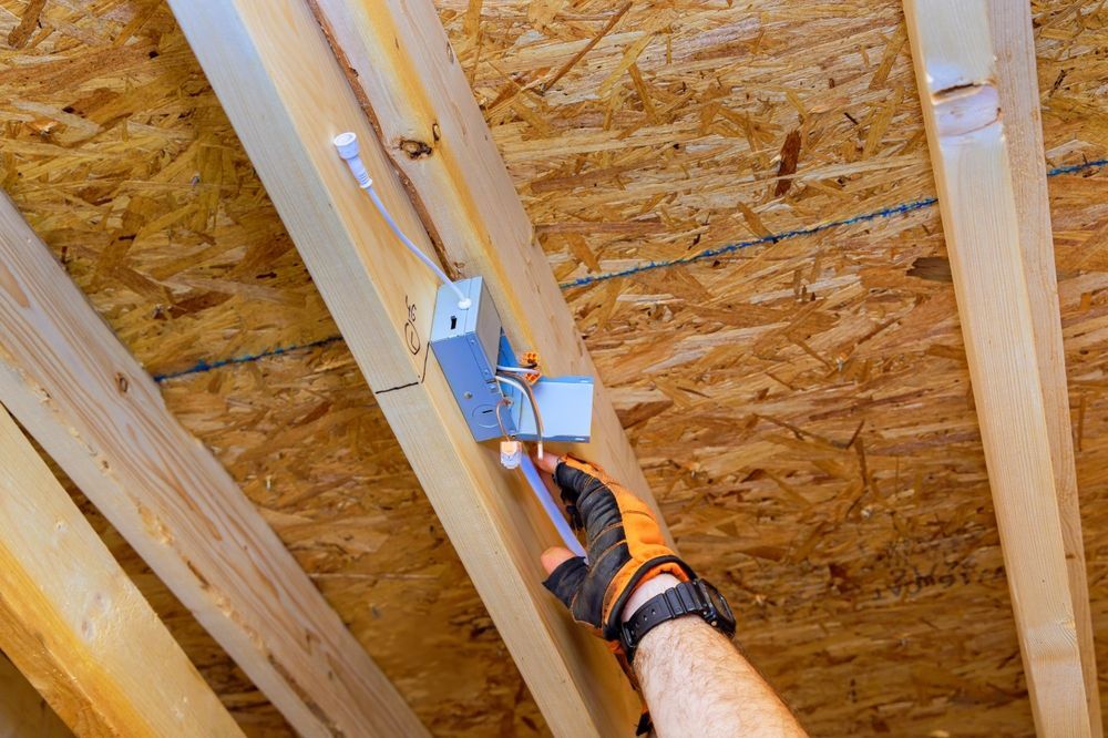 Man wearing gloves and overalls working on a white wall, using a tool.