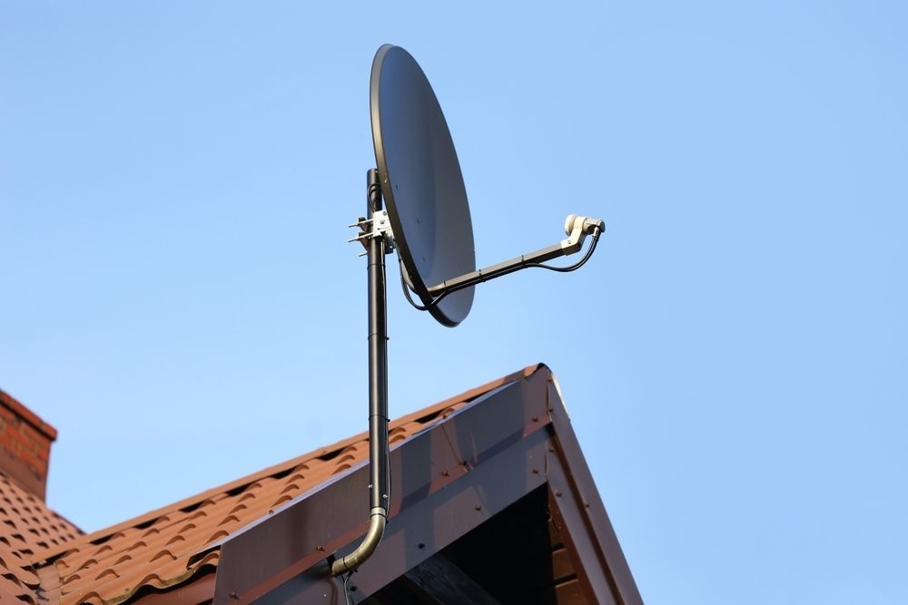 Satellite dish mounted on a brown roof against a clear blue sky.