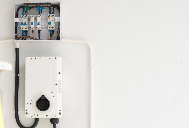 White electrical box and inverter on a white wall, with black conduit and wiring visible.