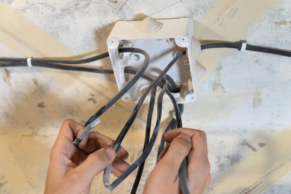 Electrician wiring an electrical outlet on a white wall inside a house.