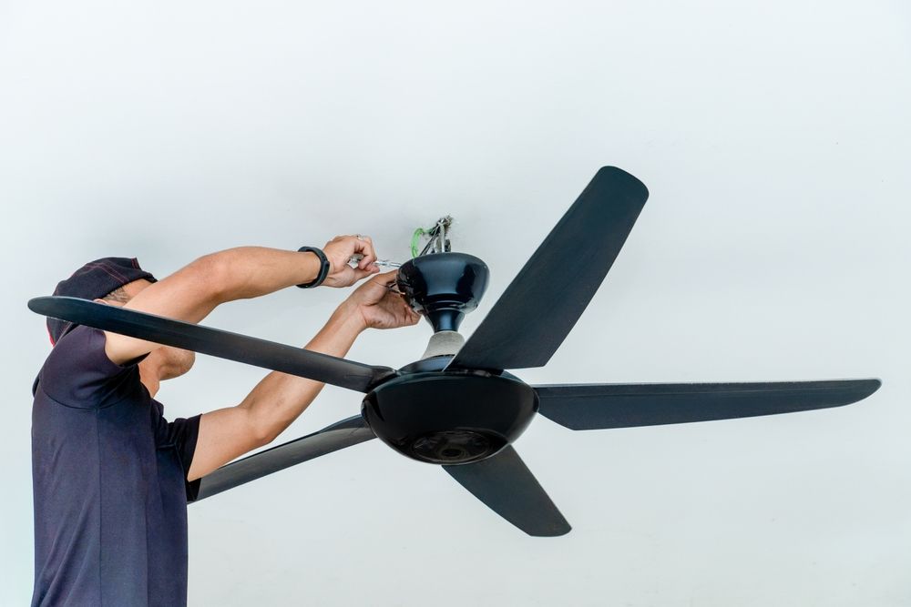Person installing a black ceiling fan, wires visible.