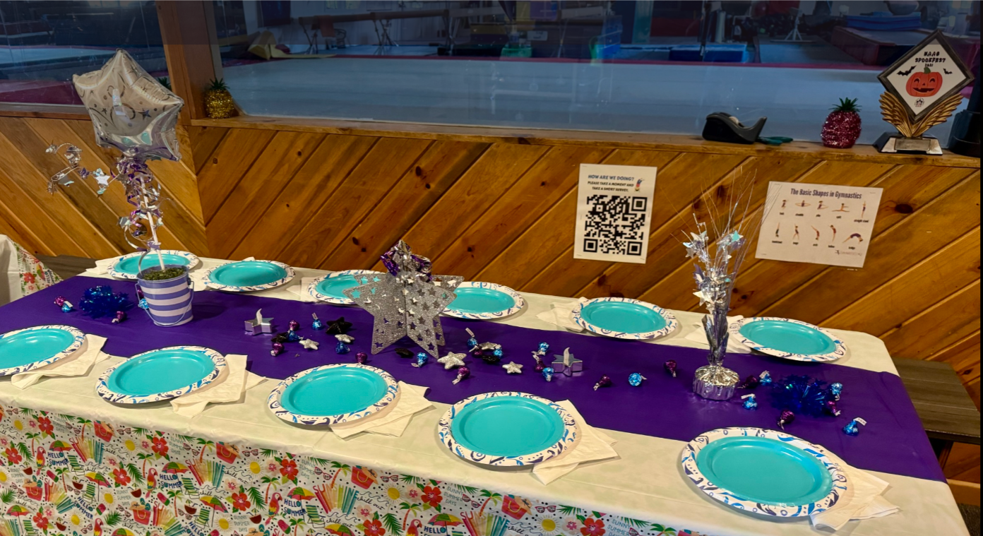 A decorated table set for a party inside a wooden building, featuring teal plates, purple and white decorations.