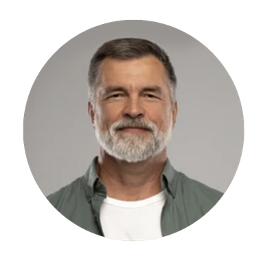 Mature man with graying hair and beard smiles, wearing a green shirt over a white t-shirt, set against a neutral gray background.