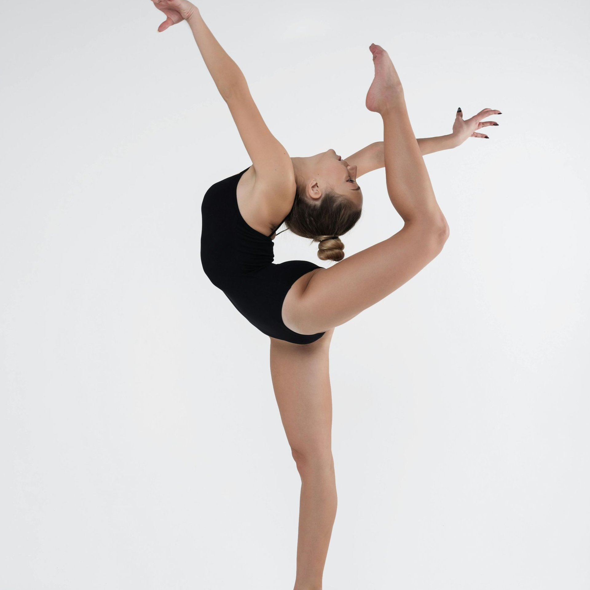 A female dancer in a black leotard balances on one leg while arching her back, raising her other leg, and extending her arms.