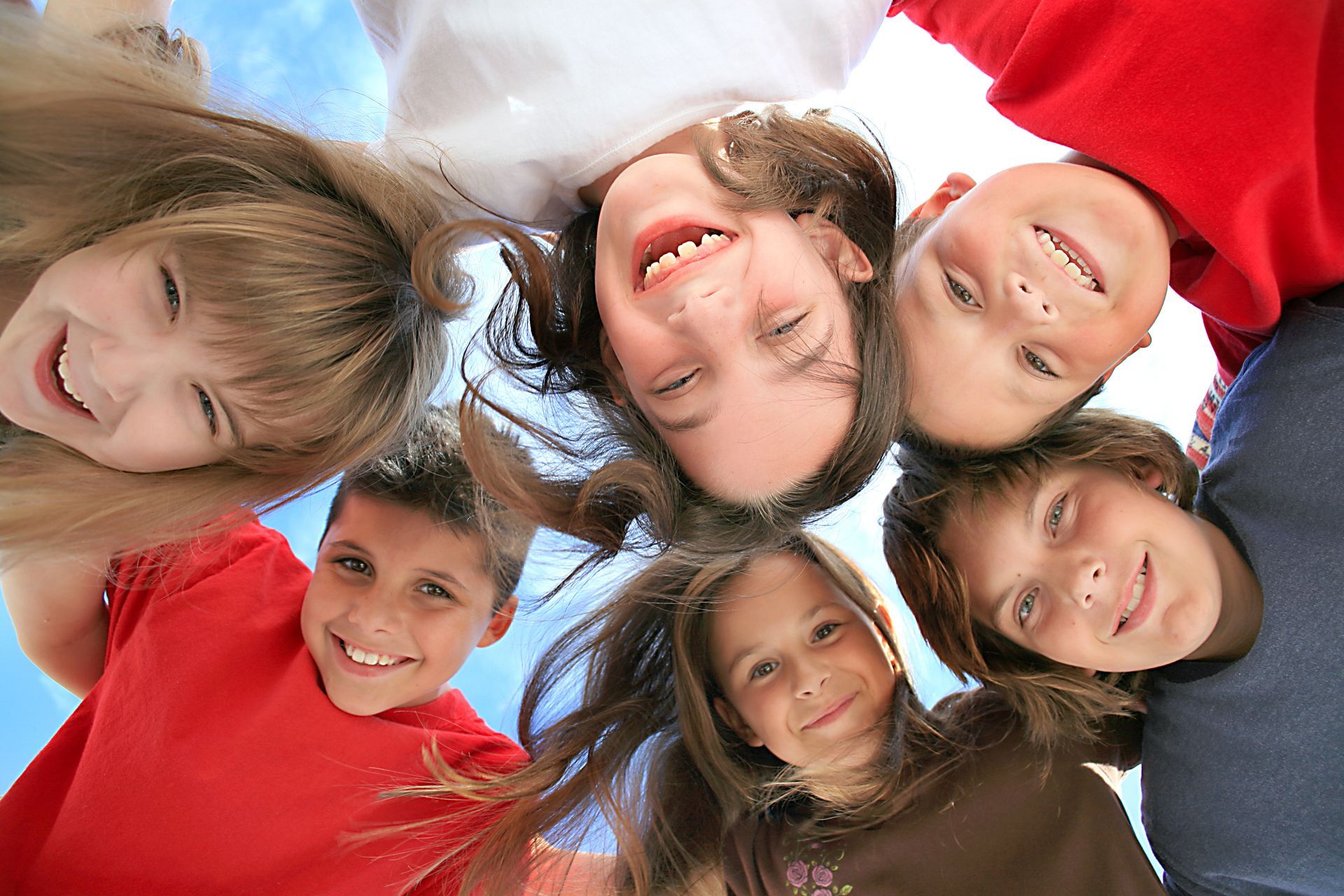 Group of smiling children looking down from a circle against a blue sky.