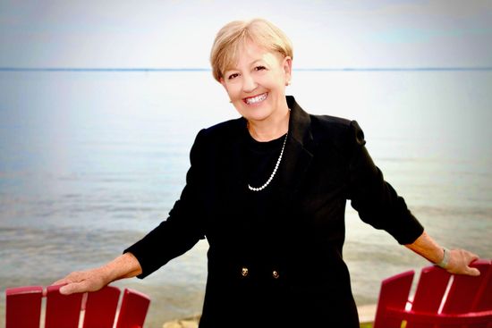 A woman is sitting at a desk with a laptop and a vase of flowers.